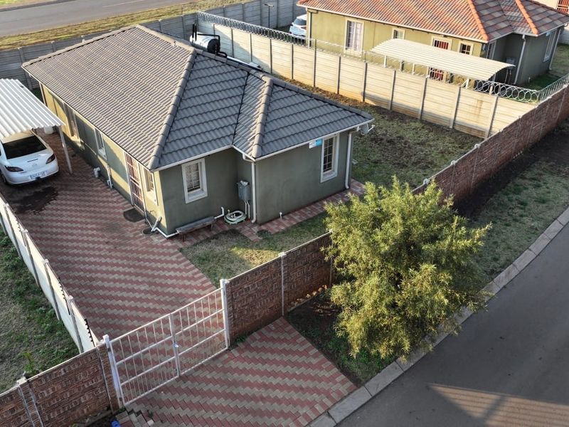 Aerial view of a residential property featuring a tiled roof, paved driveway, carport, and secure perimeter walling.