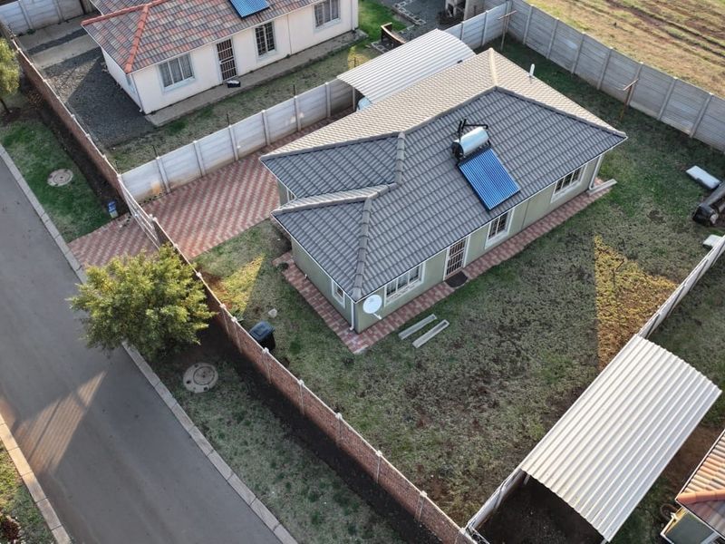 Aerial view of a residential property featuring a tiled roof with a solar water heater, paved driveway, carport, and perimeter walling.