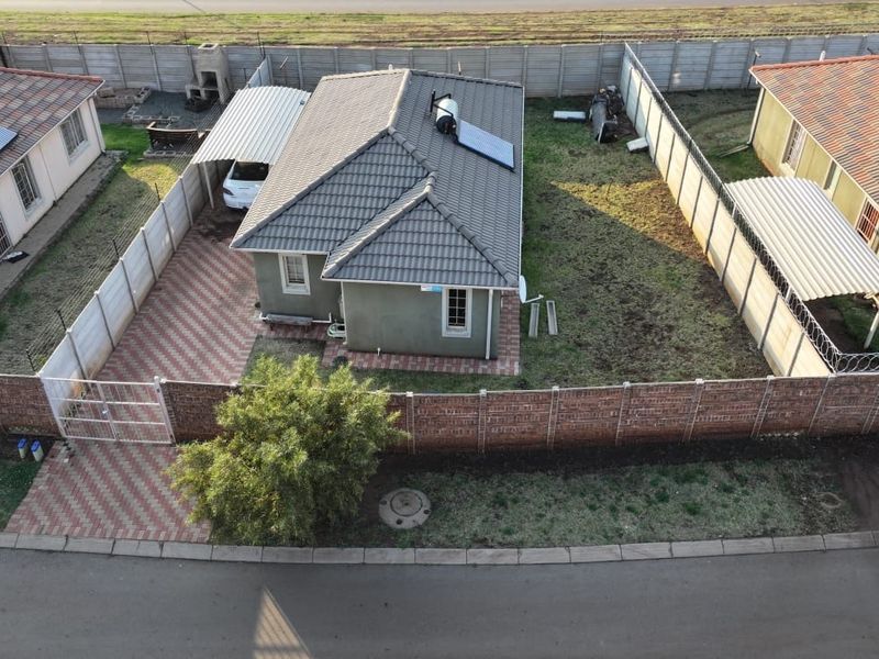 Aerial view of a residential property featuring a tiled roof with solar geyser, paved driveway, carport, and enclosed garden with precast boundary walls.