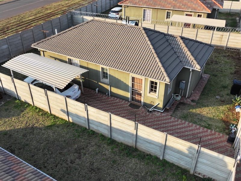 Aerial view of a residential property featuring a tiled roof, paved driveway, carport, and secure perimeter fencing.