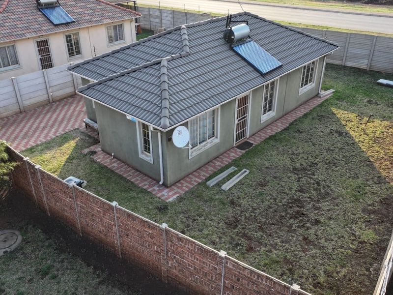 Aerial view of a detached house featuring a tiled roof with a solar water heater, paved walkways, and a fenced garden area.