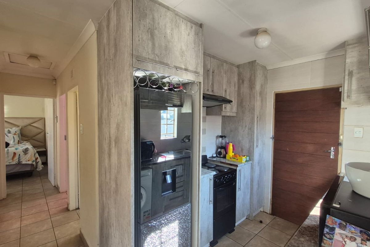 Compact kitchen featuring modern wood-look cabinetry, built-in extractor fan, and tiled flooring, with direct access to the hallway and adjacent bedroom.