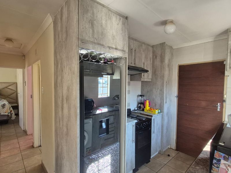Compact kitchen featuring modern wood-look cabinetry, built-in extractor fan, and tiled flooring, with direct access to the hallway and adjacent bedroom.