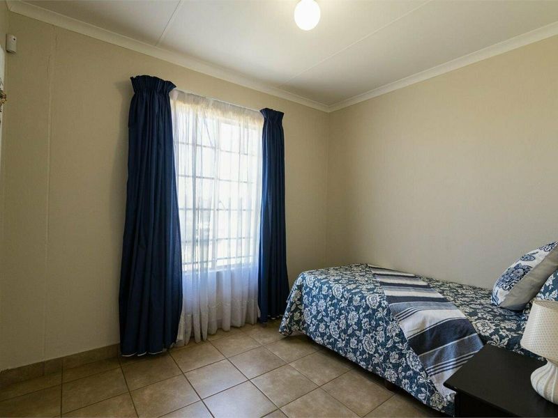 A functional bedroom featuring tiled flooring, neutral wall finishes, and a window fitted with security bars.