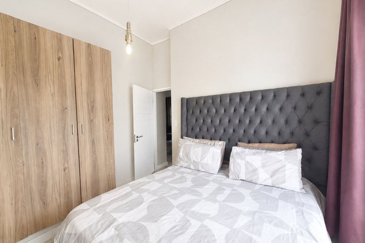 A well-maintained bedroom featuring a large built-in wood-finish wardrobe, neutral walls, and a modern pendant light fixture.