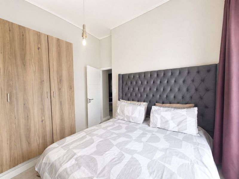 A well-maintained bedroom featuring a large built-in wood-finish wardrobe, neutral walls, and a modern pendant light fixture.