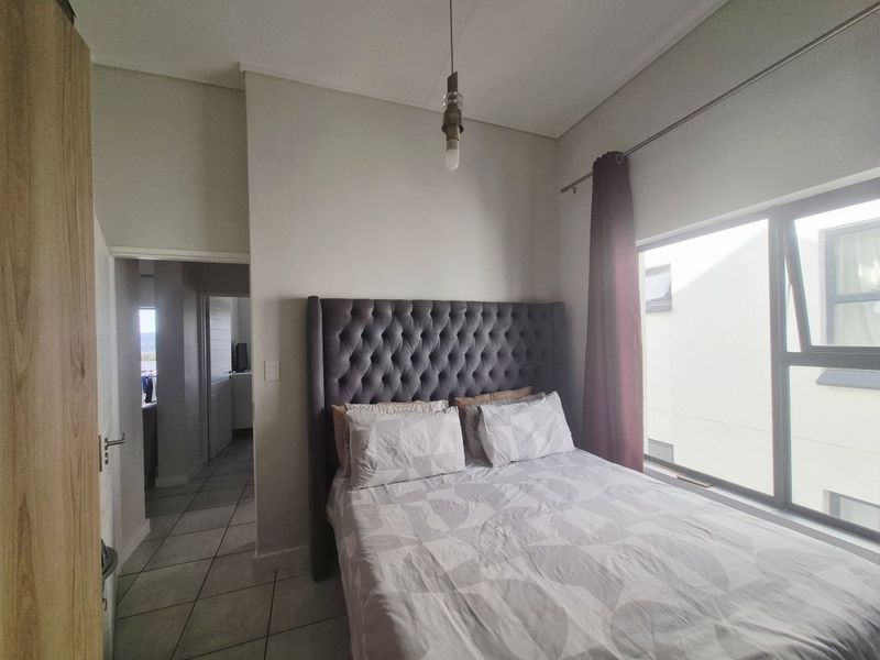 A well-lit bedroom featuring tiled flooring, a large aluminium-framed window, and built-in cupboard storage, providing a functional and comfortable living space.
