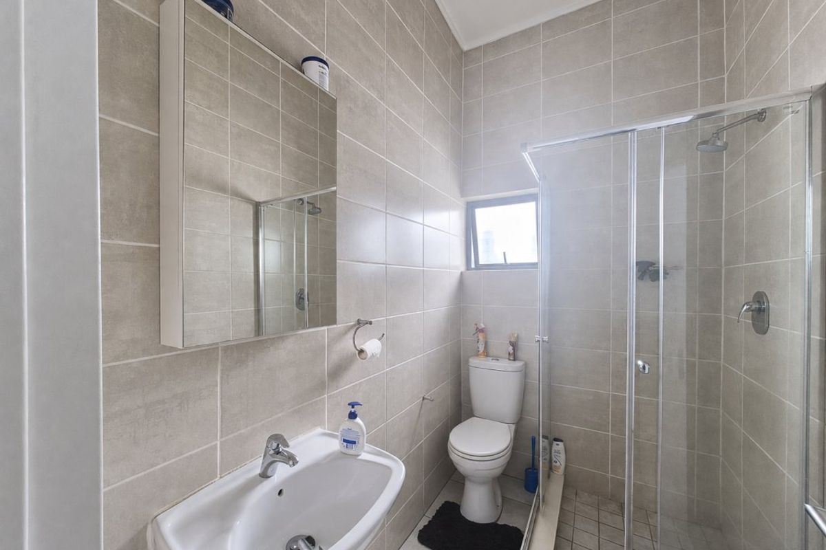 A clean, modern bathroom featuring floor-to-ceiling neutral tiling, a glass-enclosed shower, a pedestal basin, and a wall-mounted mirror cabinet.