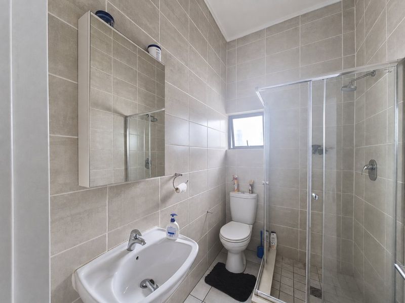 A clean, modern bathroom featuring floor-to-ceiling neutral tiling, a glass-enclosed shower, a pedestal basin, and a wall-mounted mirror cabinet.