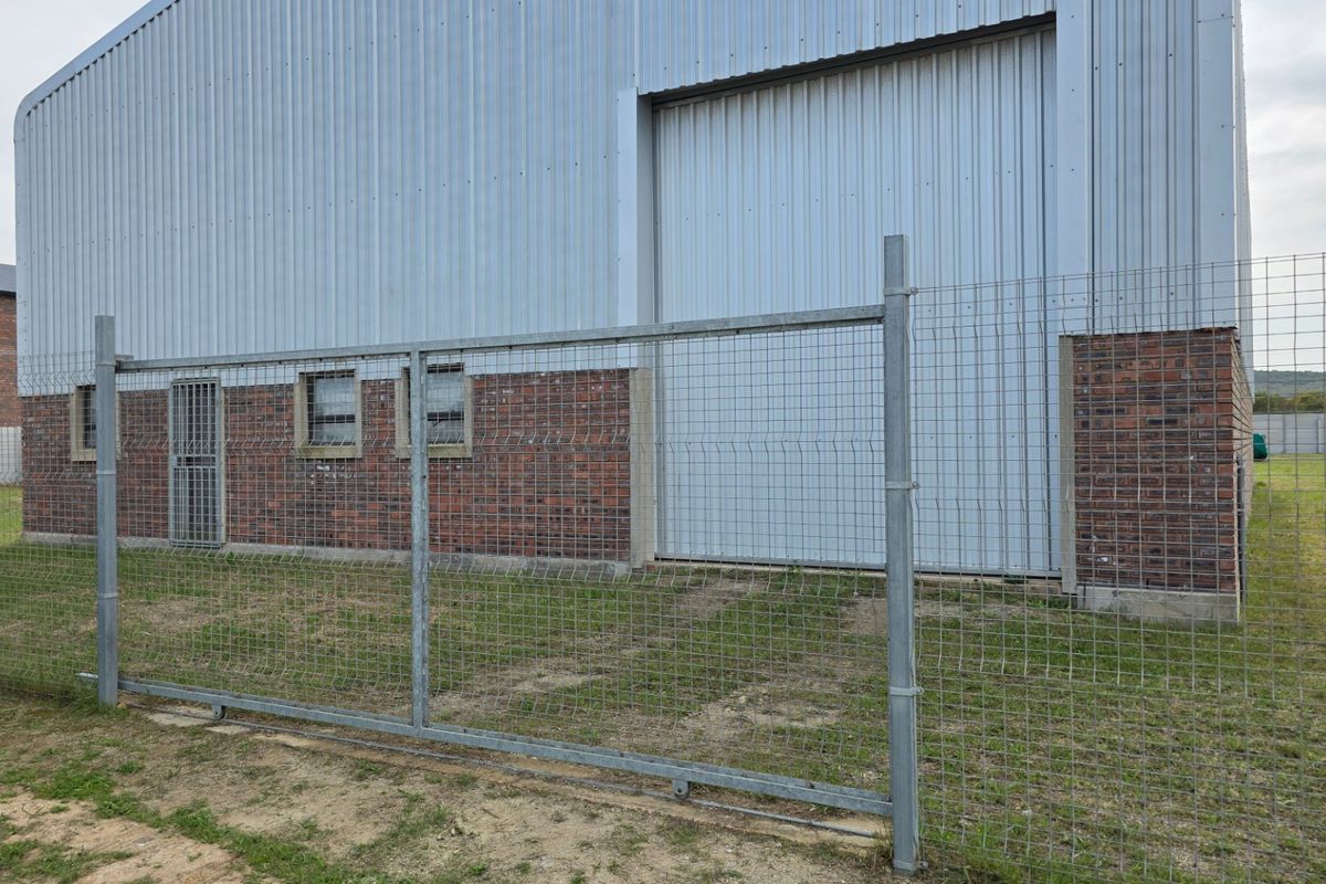 Rear view of an industrial warehouse featuring corrugated metal cladding, a large roller door, and secure perimeter mesh fencing.