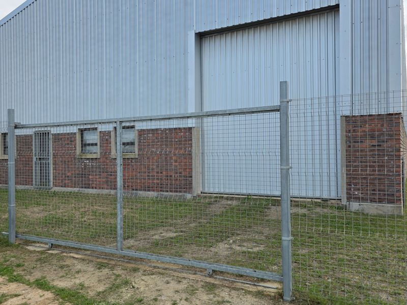 Rear view of an industrial warehouse featuring corrugated metal cladding, a large roller door, and secure perimeter mesh fencing.