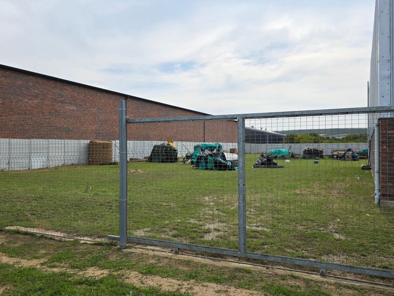 A fenced rear yard area featuring a combination of brick and precast concrete boundary walls, adjacent to an industrial building with metal cladding.