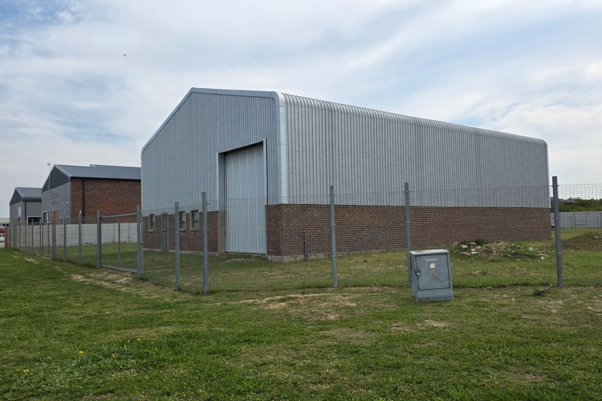 Rear view of an industrial warehouse featuring corrugated metal cladding, a brick base, and a large roller door, secured by perimeter fencing.
