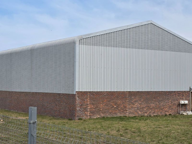 Rear view of an industrial warehouse building featuring a brick base, corrugated metal upper walls, and a gabled roof structure.
