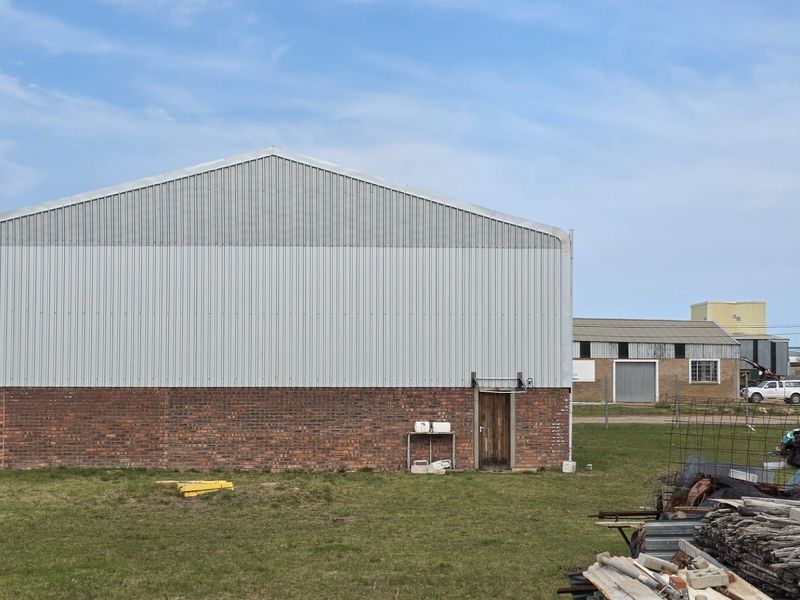 Rear view of an industrial warehouse building featuring a combination of brick masonry and corrugated metal cladding with a single access door.