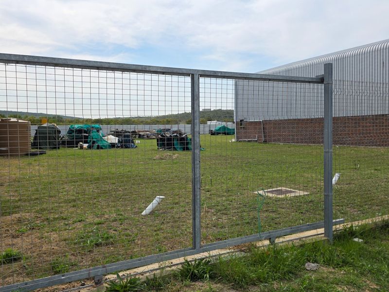 Rear industrial yard area featuring galvanized wire mesh fencing, metal cladding, and a water storage tank on a grassed plot.