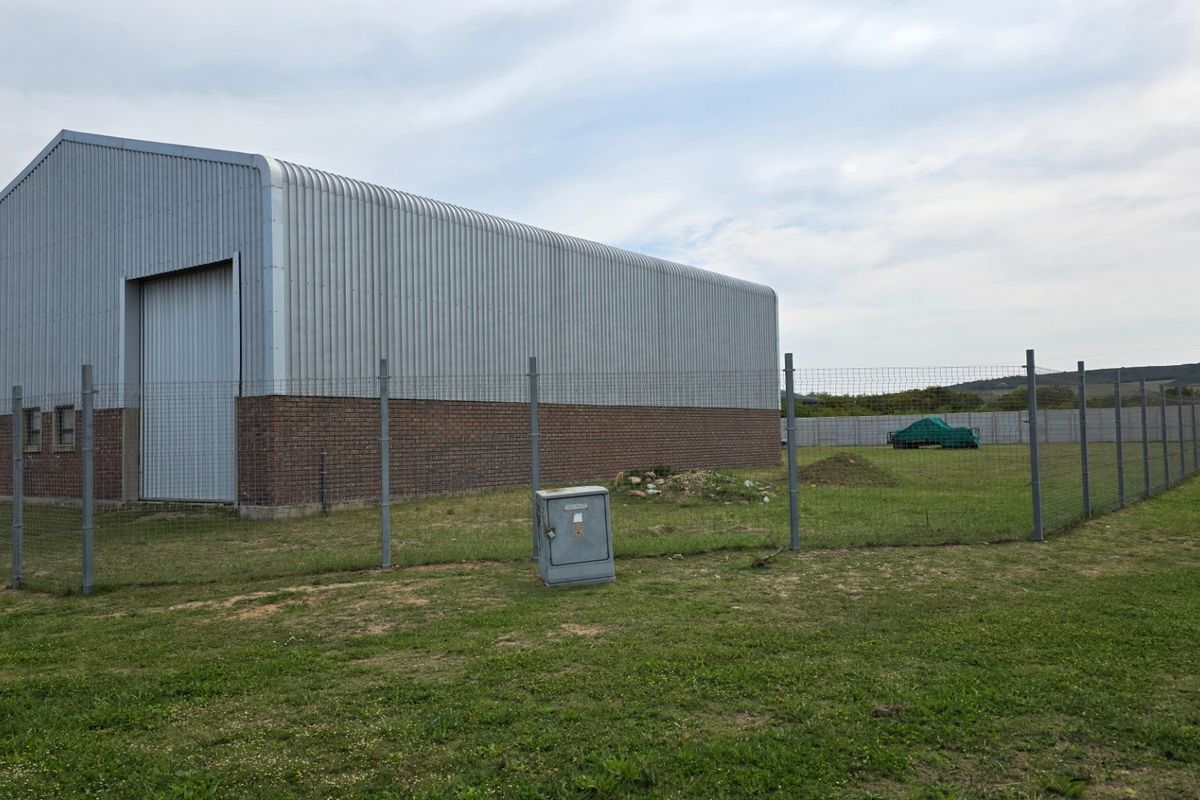 Rear view of an industrial warehouse featuring corrugated metal cladding, a brick base, and a secure perimeter fence.