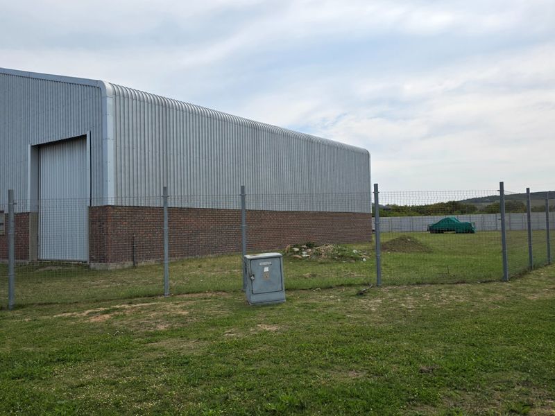 Rear view of an industrial warehouse featuring corrugated metal cladding, a brick base, and a secure perimeter fence.