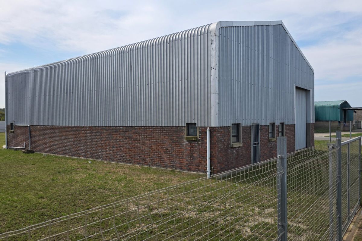 Industrial warehouse building featuring a combination of brick masonry and corrugated metal cladding with a secure roller shutter entrance.