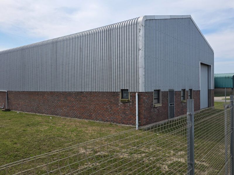 Industrial warehouse building featuring a combination of brick masonry and corrugated metal cladding with a secure roller shutter entrance.