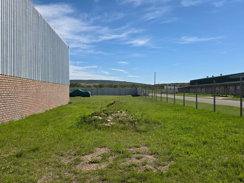 Rear exterior view of an industrial property featuring corrugated metal and brick wall construction with surrounding wire mesh fencing and open grass area.
