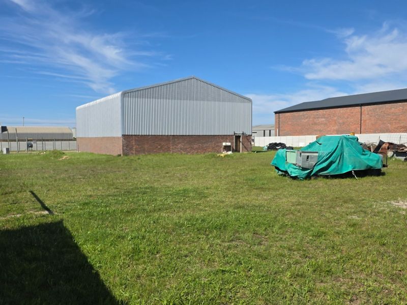 Rear view of an industrial property featuring a metal-clad warehouse structure with brick base and surrounding open yard space.