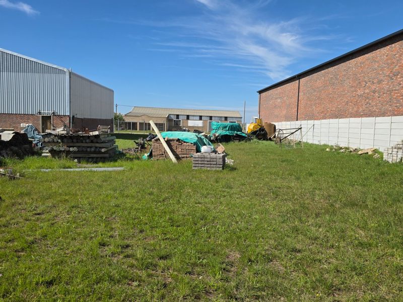 Rear yard area of an industrial property featuring brick and metal-clad warehouse structures with an open grassed space and boundary walling.