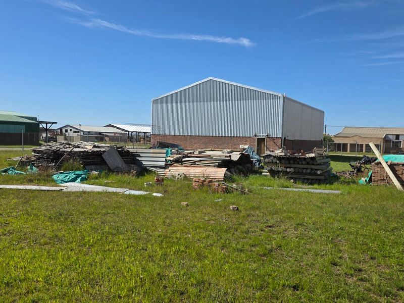 Rear view of an industrial warehouse building featuring corrugated metal cladding and a brick base, situated on a large open plot.