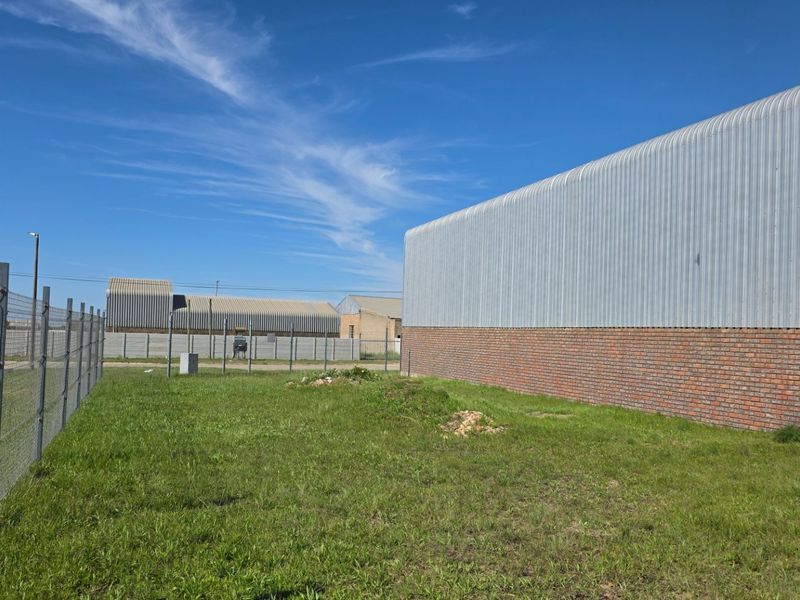Exterior view of an industrial building featuring corrugated metal cladding, a brick base, and secure perimeter wire fencing.