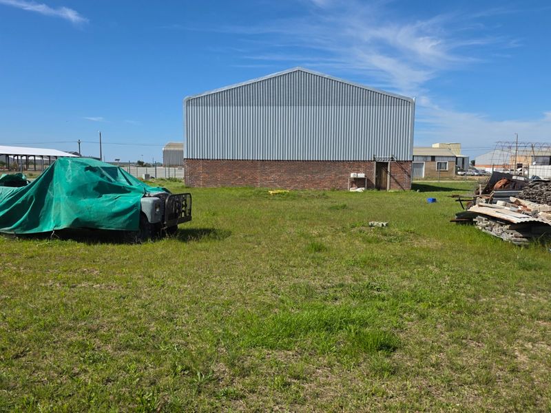 Rear view of an industrial warehouse building featuring corrugated metal siding and a brick foundation set on a large open plot.