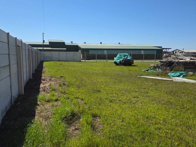 Open industrial yard area featuring a precast concrete boundary wall, chain link fencing, and an expansive grass lawn.