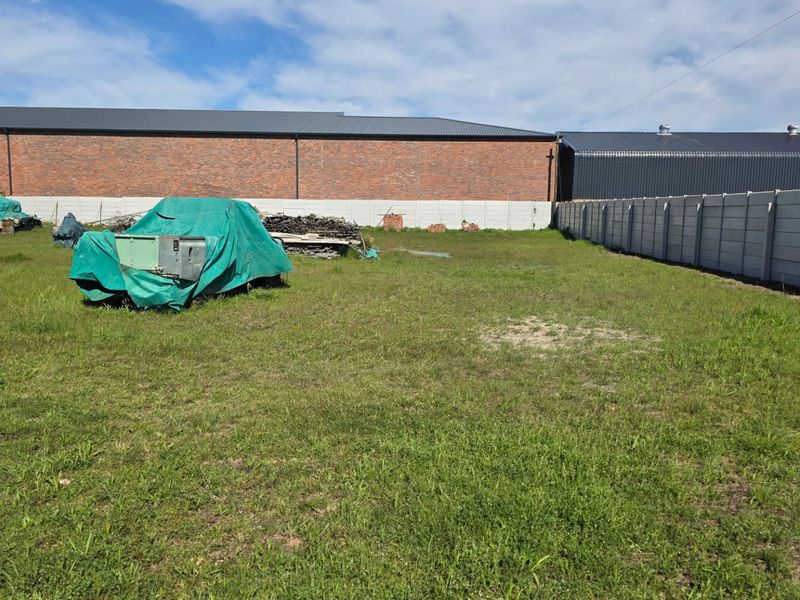 A spacious open yard area featuring a precast concrete boundary wall and views of an adjacent industrial building with a metal roof.