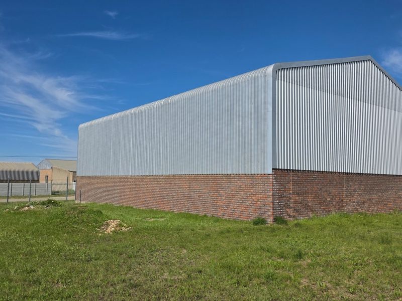 Rear view of an industrial warehouse building featuring a brick base and corrugated metal cladding under a pitched roof.