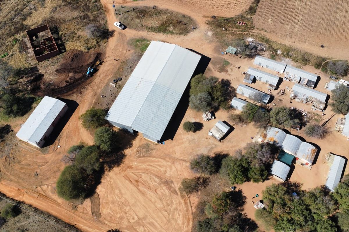 Aerial view of a farm property featuring a large central metal shed, multiple outbuildings, and extensive unpaved grounds.