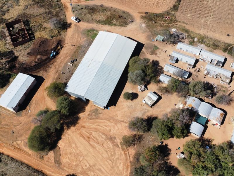 Aerial view of a farm property featuring a large central metal shed, multiple outbuildings, and extensive unpaved grounds.