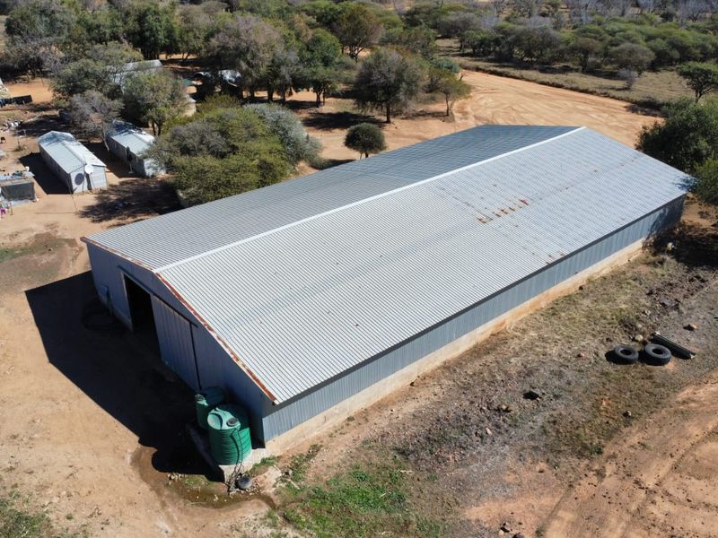 Aerial view of a large agricultural shed or barn featuring a corrugated metal roof and exterior siding, situated on a rural farm property.