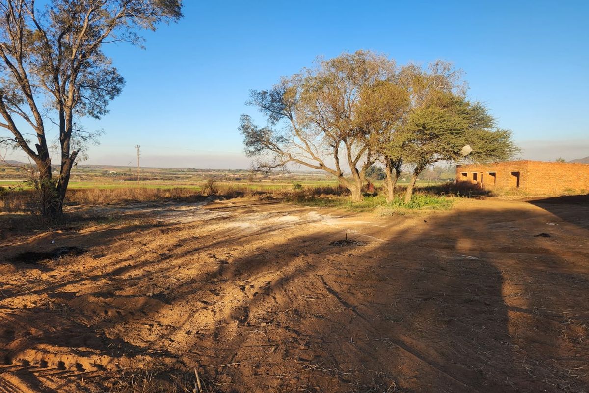 Expansive rural land featuring mature trees and an unfinished brick structure, offering significant potential for development or landscaping.