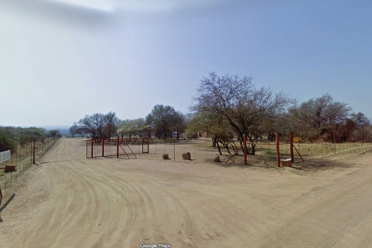 A view of the farm entrance featuring a metal gate, wire fencing, and a dirt access road leading into the property.