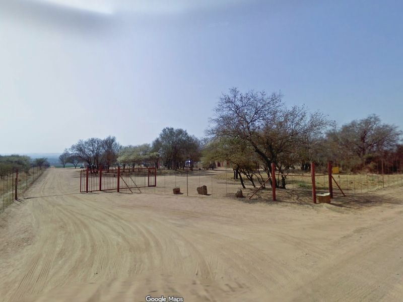 A view of the farm entrance featuring a metal gate, wire fencing, and a dirt access road leading into the property.