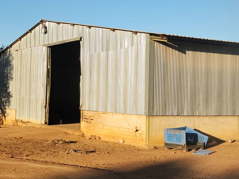 A large agricultural utility shed featuring corrugated metal siding and a concrete foundation, suitable for storage or farm operations.