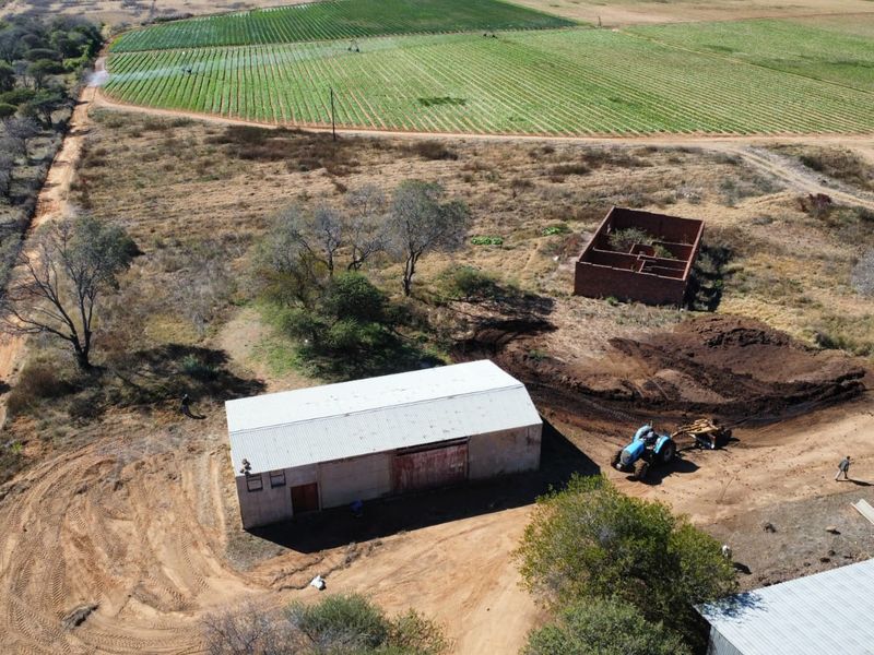 Aerial view of a farm property featuring a large metal-roofed barn, a dilapidated brick structure, and surrounding agricultural fields.