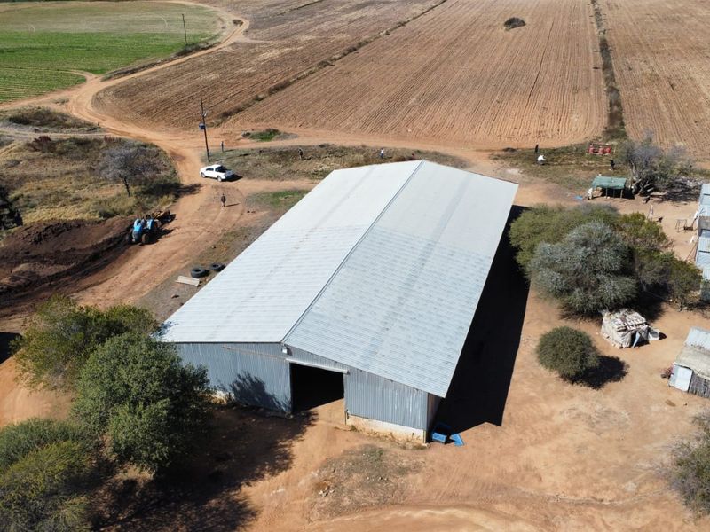 Aerial view of a large corrugated metal farm shed situated on a rural property with surrounding dirt tracks and auxiliary outbuildings.