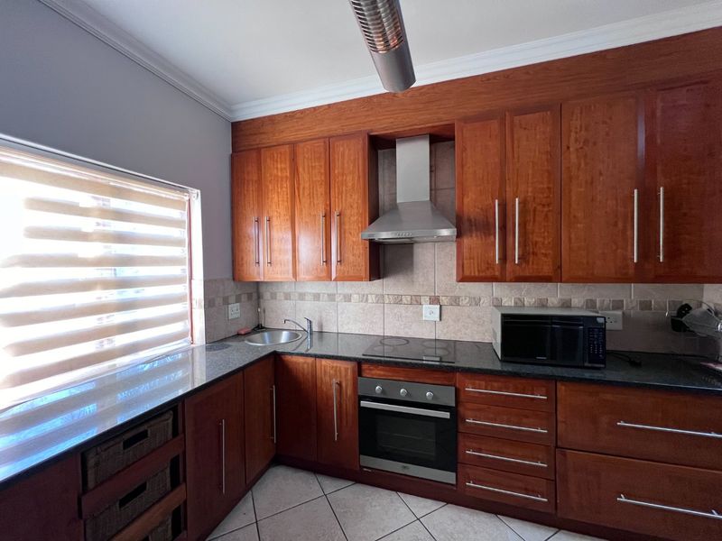 A functional kitchen featuring warm-toned wooden cabinetry, granite countertops, a stainless steel extractor fan, built-in oven, and a tiled backsplash.