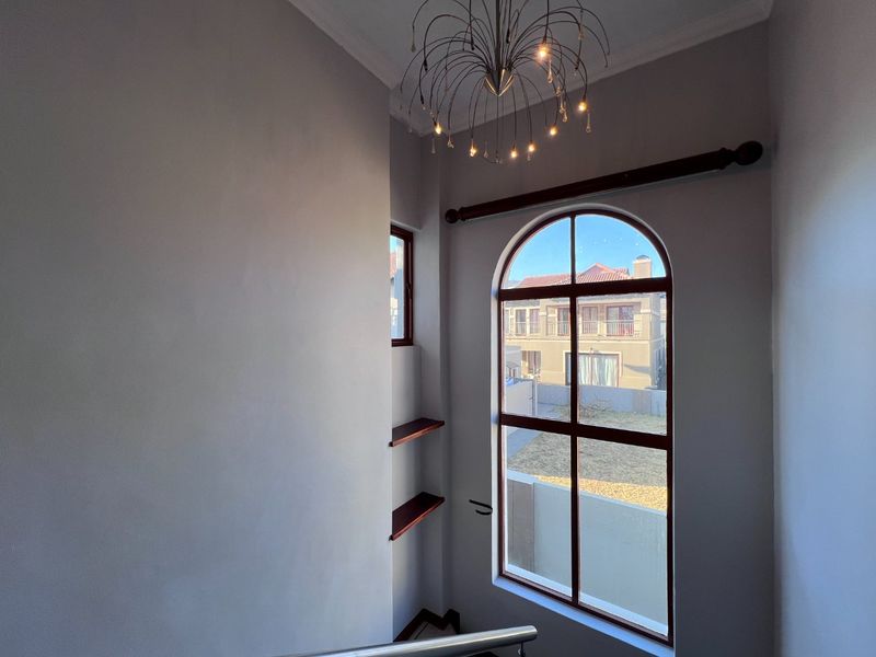 A bright hallway featuring an elegant arched window, built-in wooden shelving, and a modern chandelier, providing a clean and well-maintained transition space.