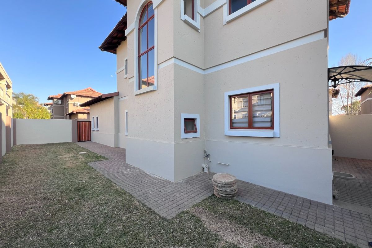 Rear view of the property featuring a paved walkway, well-maintained lawn, and exterior wall finishes with arched window detailing.