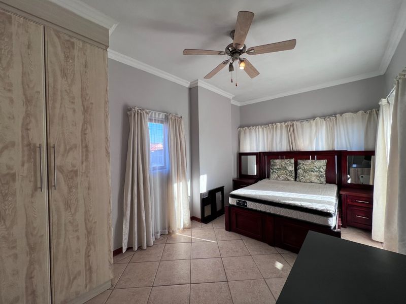 Spacious bedroom featuring tiled flooring, a ceiling fan, and a large built-in wardrobe with light wood finish.