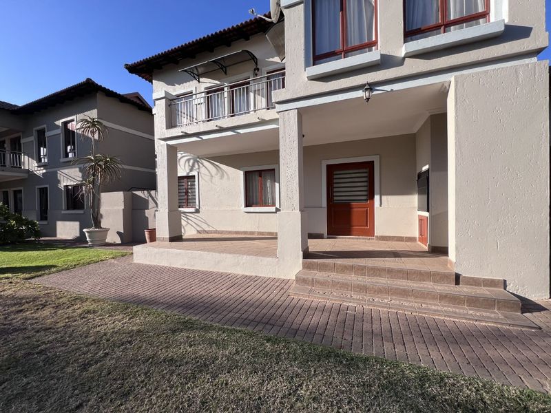 Rear view of the property featuring a covered tiled patio, brick paved area, and an upper-level balcony with a built-in braai.
