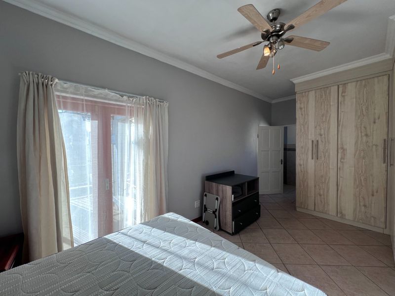 Spacious bedroom featuring tiled flooring, built-in wooden cupboards, a ceiling fan, and direct access to an outdoor area through sliding glass doors.