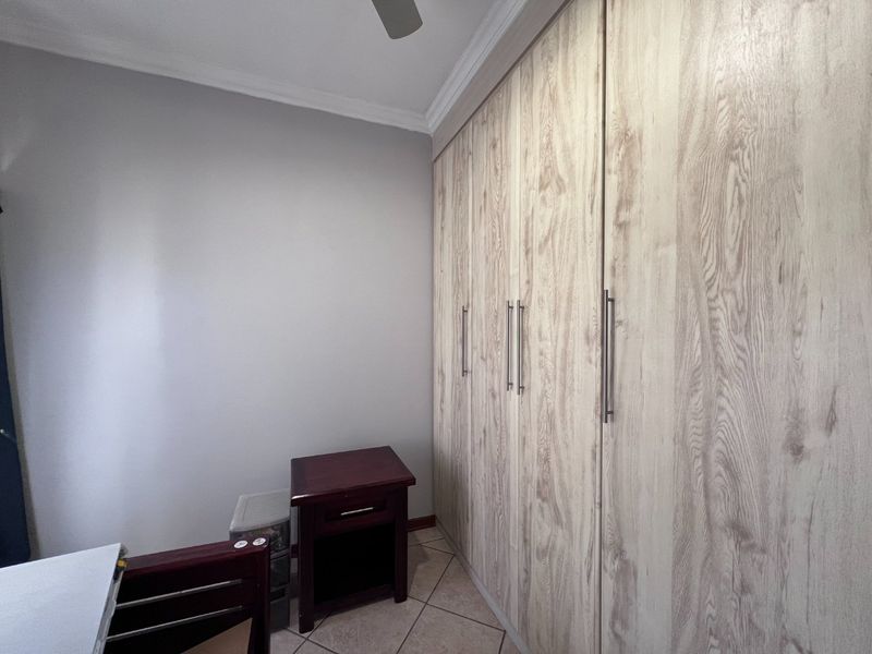 A bedroom featuring light wood-grain built-in cupboards, tiled flooring, and a ceiling fan.