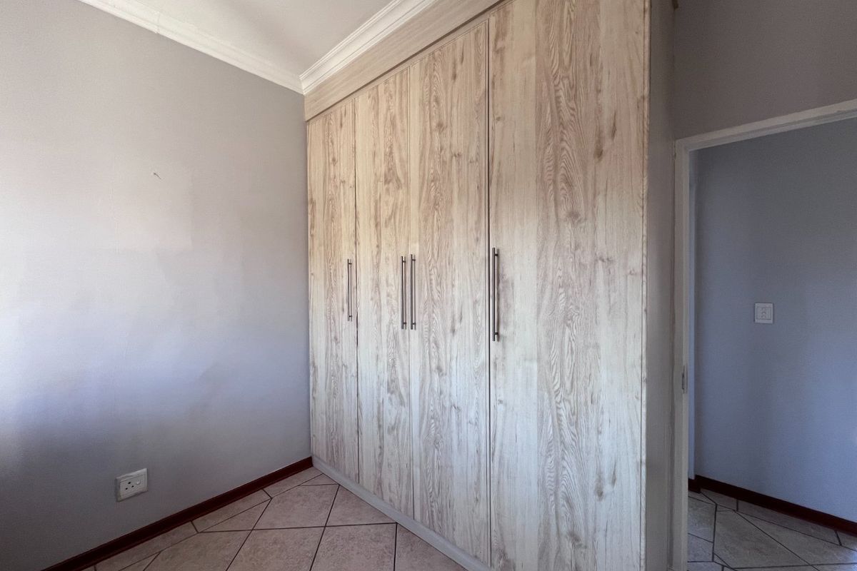 A clean, empty bedroom featuring light wood-grain built-in cupboards, neutral wall finishes, and tiled flooring.